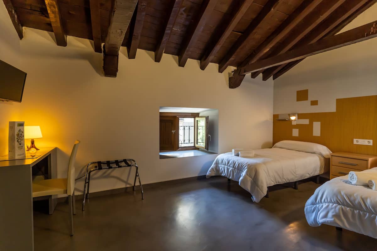 A room with two beds, a desk with a lamp, a chair, and a window with a view.