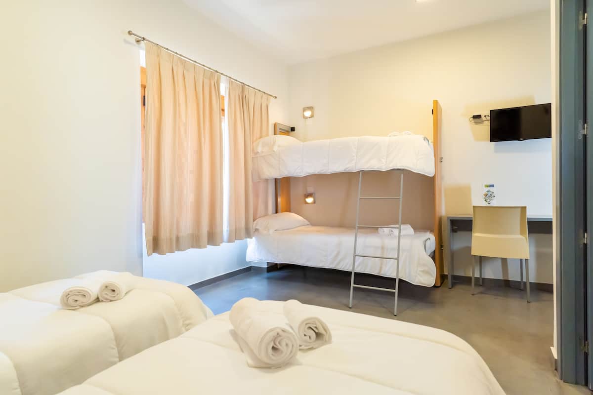 A hotel room with two beds, a desk, a chair, and a TV on the wall.