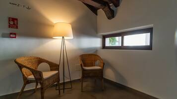 Zwei Korbstühle mit weißen Kissen, eine Stehlampe, ein Fenster mit Blick und ein Rauchmelder-Schild an der Wand.