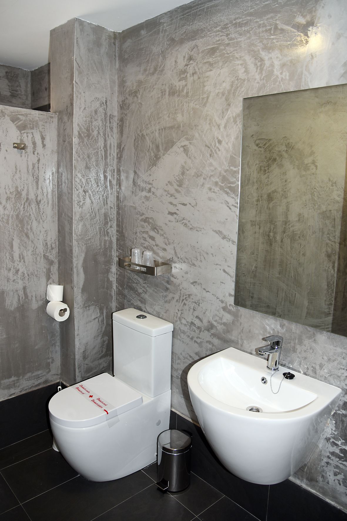 Een moderne badkamer met toilet, bidet en wastafel, marmeren wanden en een grote spiegel.