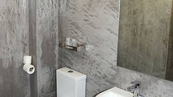 A modern bathroom with a toilet, bidet, and sink, marble walls, and a large mirror.