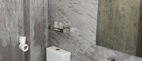 Een moderne badkamer met toilet, bidet en wastafel, marmeren wanden en een grote spiegel.
