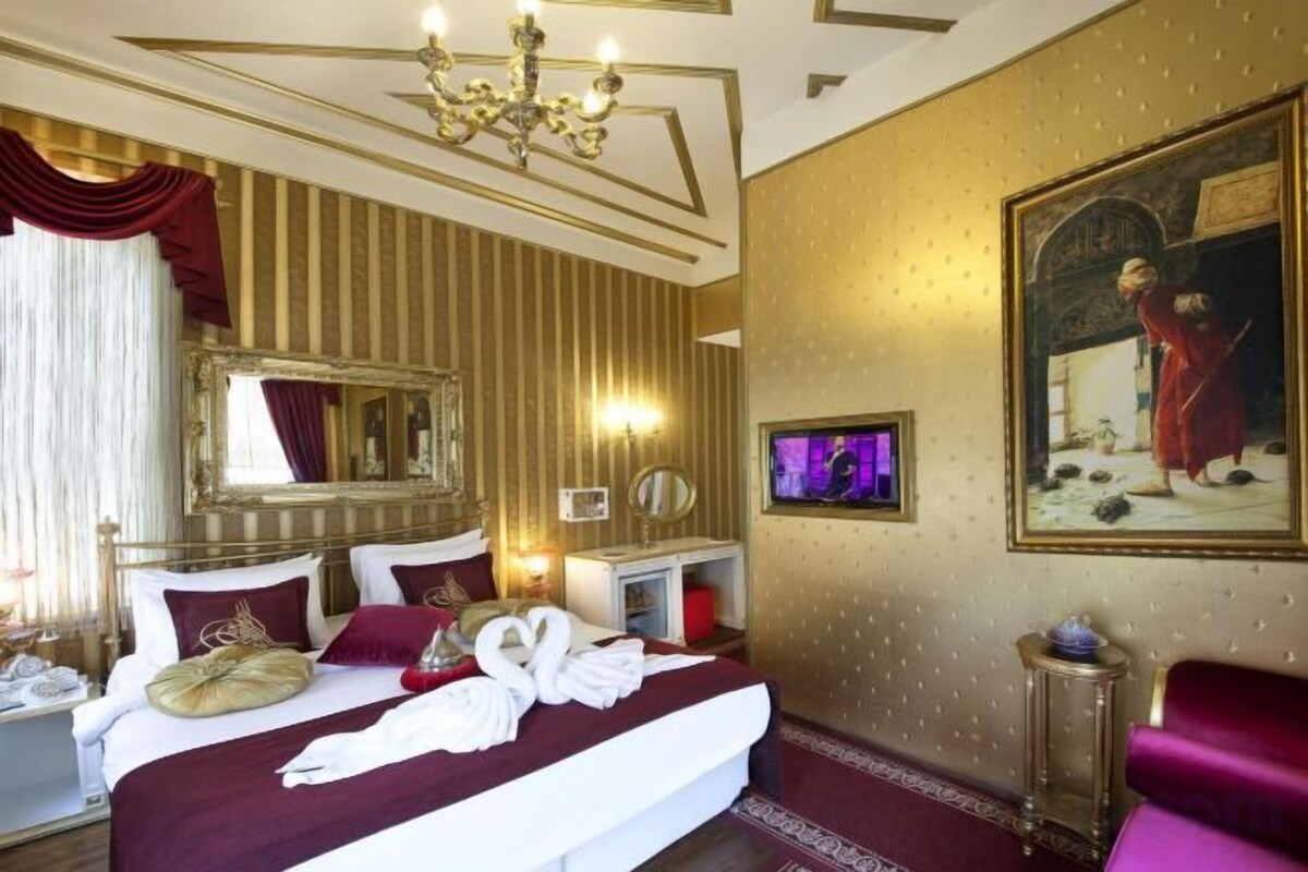 A hotel room with a large bed, a chandelier, a painting, and a television.