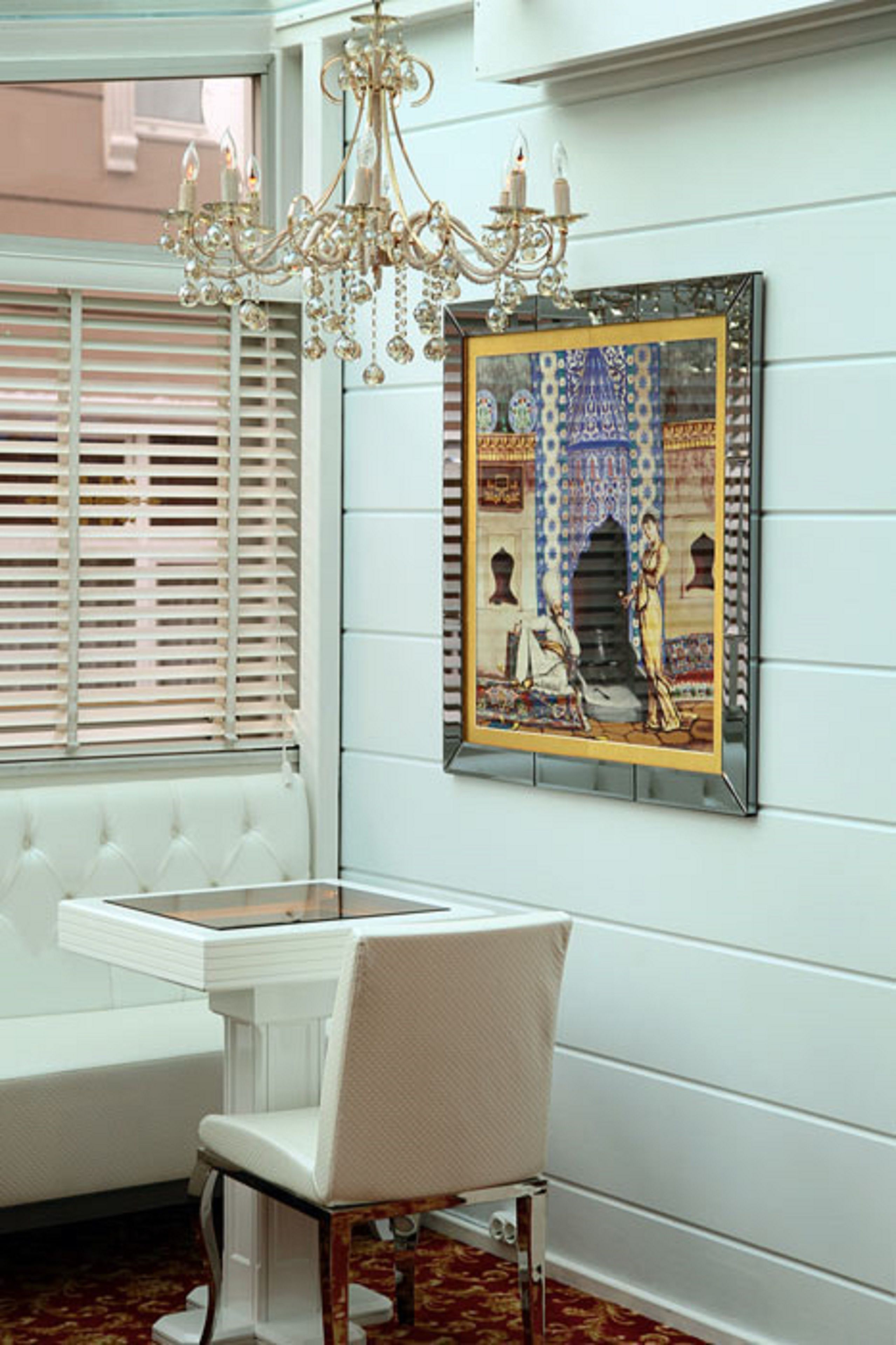 A room with a white upholstered bench, a white table, a chandelier, and a framed artwork on the wall.