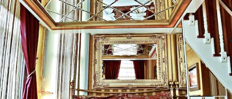 A luxurious bedroom with a large bed, ornate gold-framed mirror, and a balcony with a view.