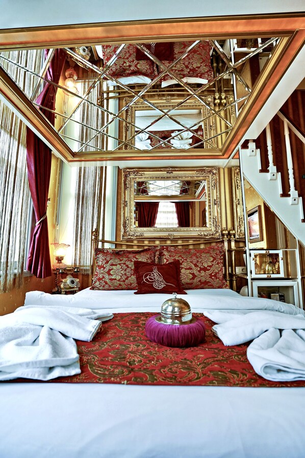 A luxurious bedroom with a large bed, ornate gold-framed mirror, and a balcony with a view.