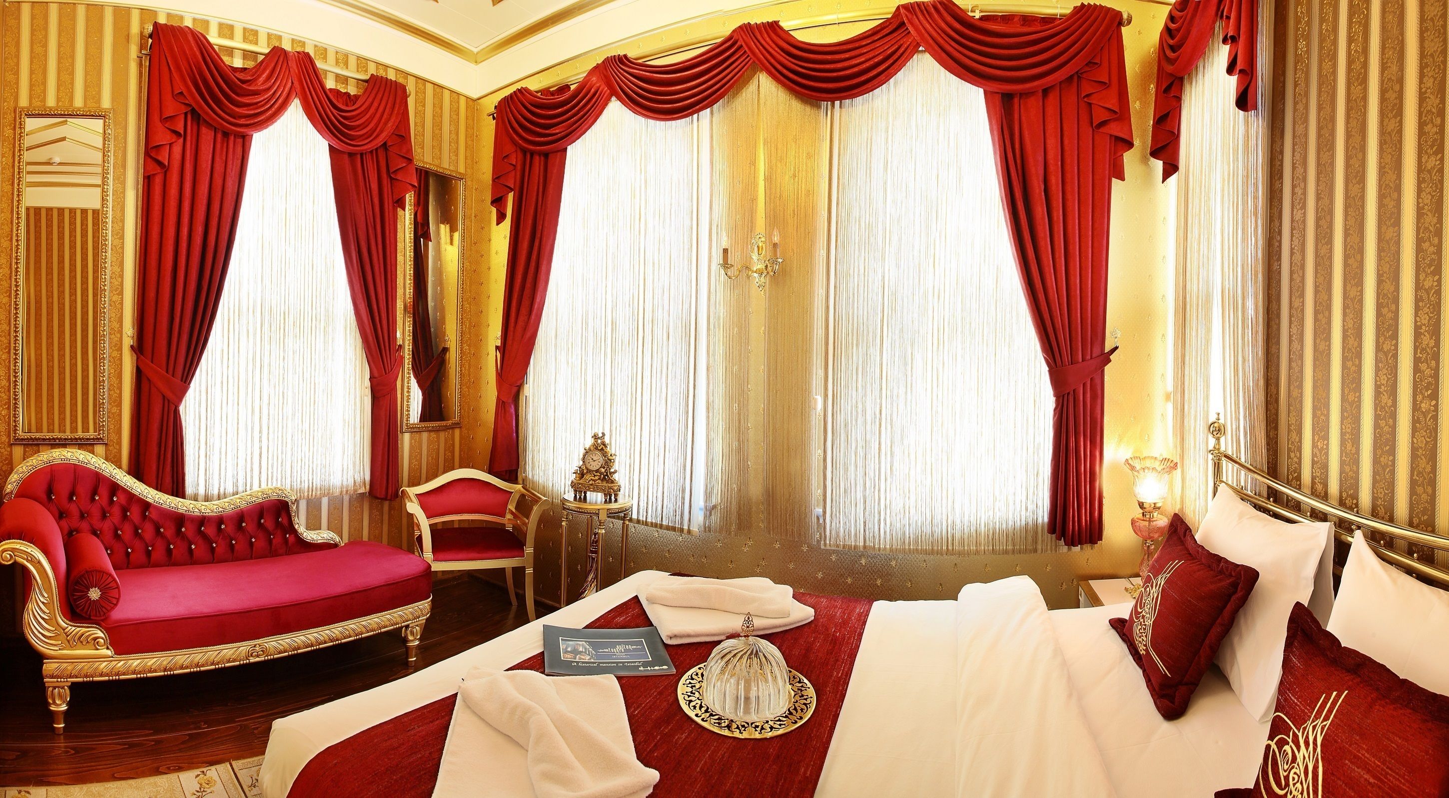 Ein luxuriöses Schlafzimmer mit einem roten Sofa, einem Bett mit weißen Bettwäsche und roten Vorhängen.