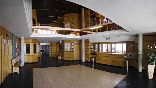 A spacious lobby with wooden paneling, a central open area, and a mezzanine level. - Albergue Inturjoven Sierra Nevada - Hostel (Monachil)