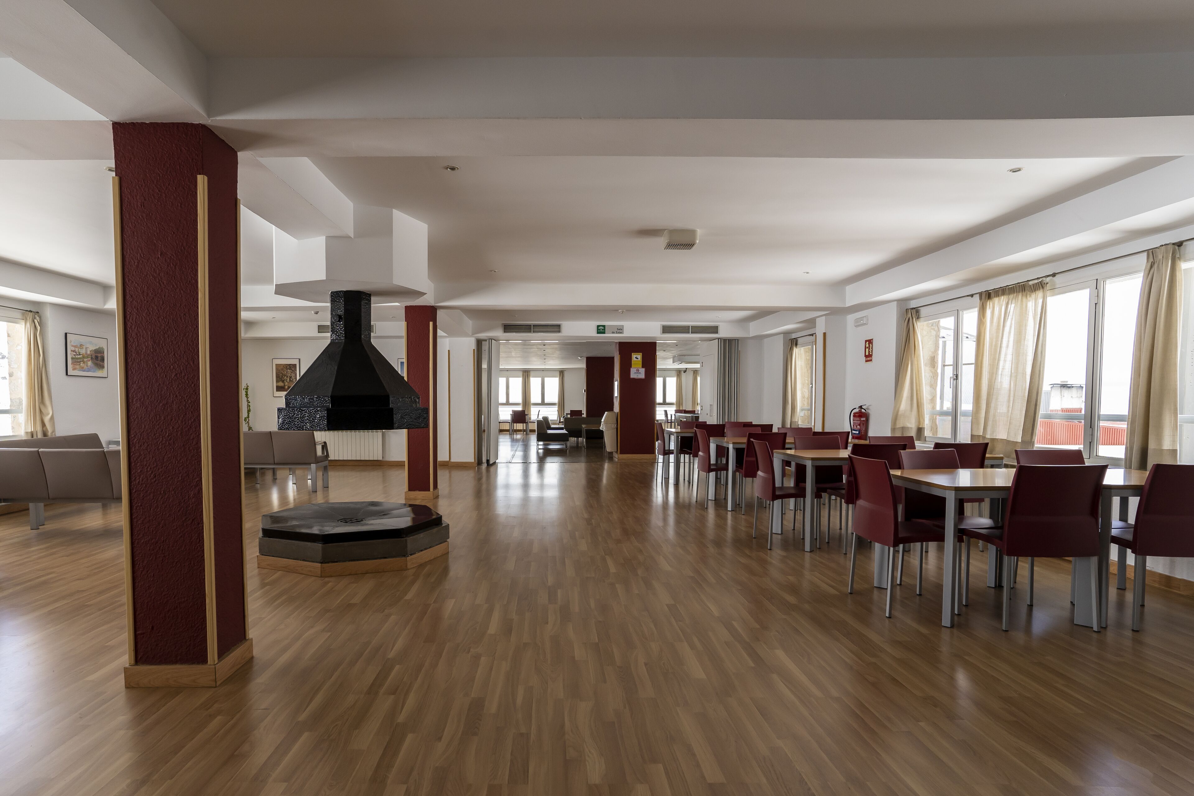 Un'ampia sala da pranzo con pavimento in legno, sedie rosse e tavoli.