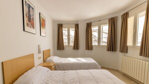 A hotel room with two beds, a wooden headboard, a bedside table, a window with curtains, and a wall-mounted telephone. - Albergue Inturjoven Sierra Nevada - Hostel (Monachil)