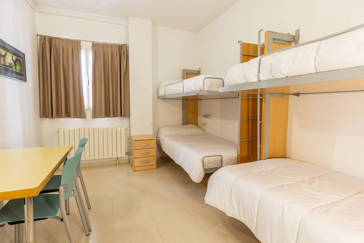 A dormitory room with bunk beds, a desk, and a chair.