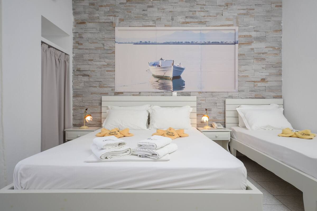 A hotel room with a large bed, two bedside tables, a nightstand, and a painting of a boat on the wall.