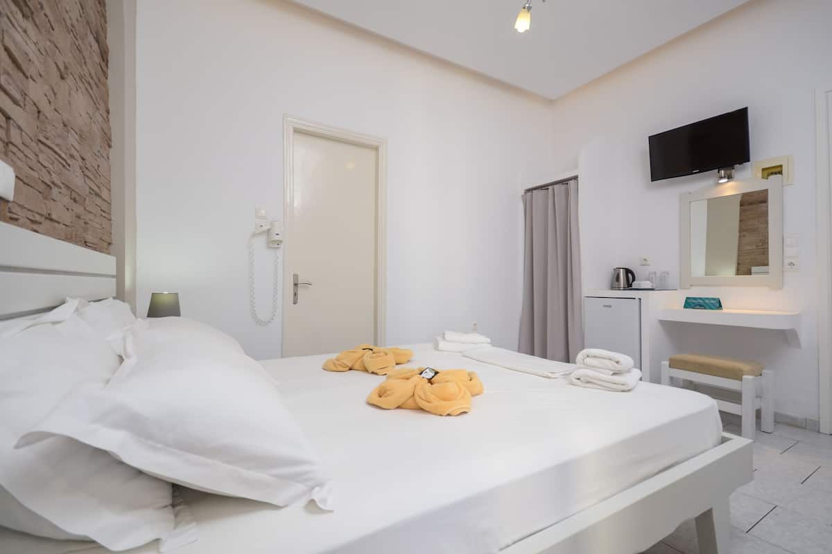A hotel room with a bed, a desk, a mirror, and a television.