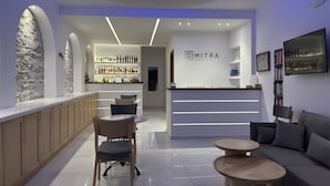 Un hall d’hôtel moderne comprenant un comptoir d’accueil, un espace salon et un bar avec un mur en pierre en arrière-plan.