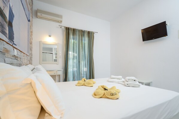 Une chambre d’hôtel équipée d’un lit, d’un bureau, d’un miroir, d’un téléviseur à écran plat et d’une fenêtre avec des rideaux.