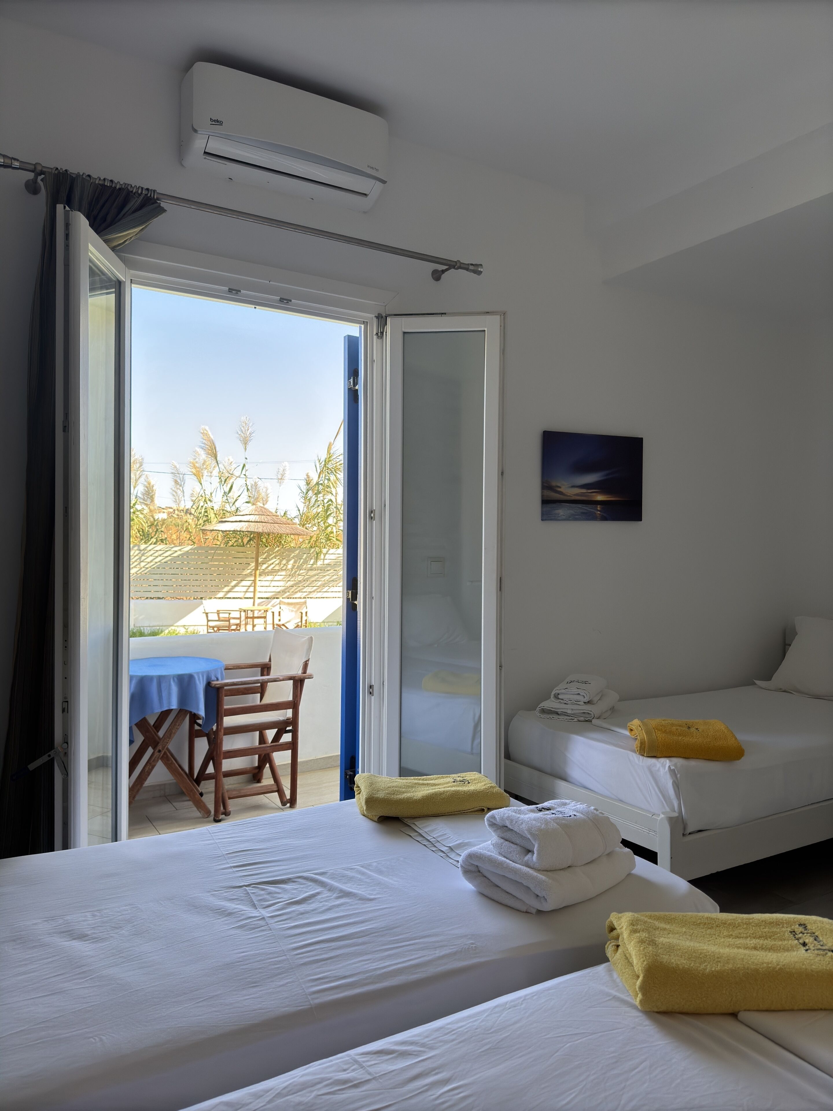 A hotel room with two beds, a balcony with a table and chairs, and an air conditioning unit.