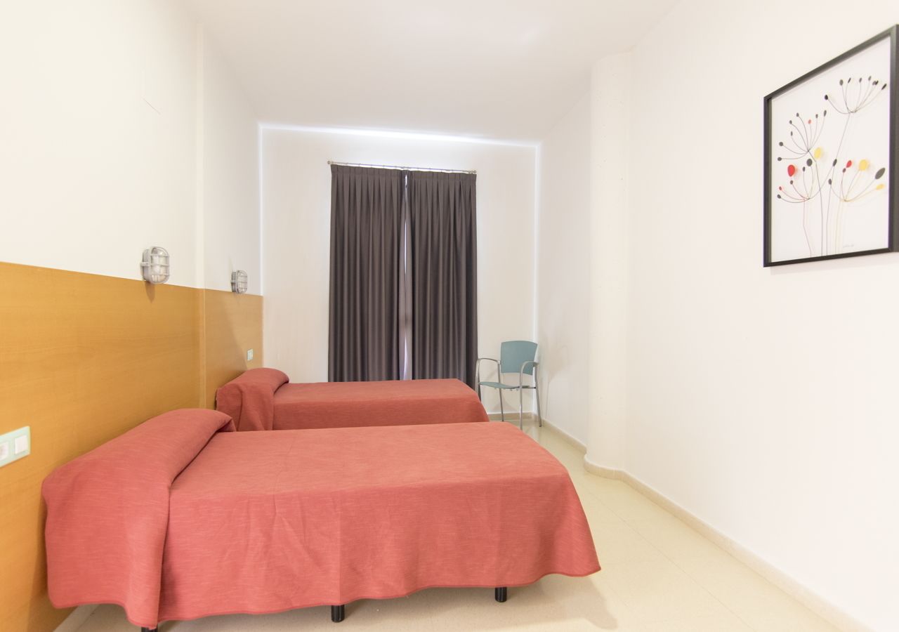 A hotel room with two beds, a chair, a window with curtains, and a framed picture on the wall.