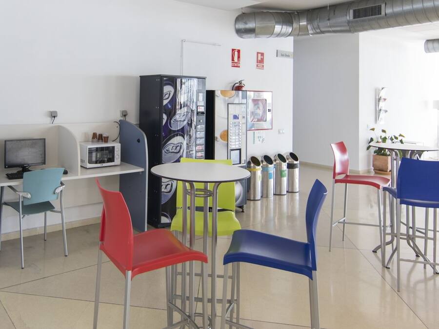 Un espacio de oficina moderno con una mesa blanca, sillas coloridas, una máquina expendedora y un microondas.