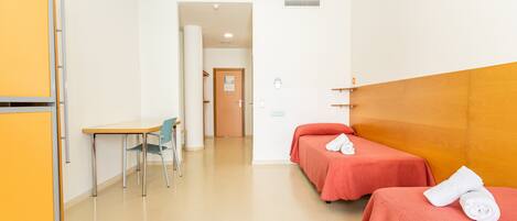 Habitación de hotel con dos camas, un escritorio, una silla y la puerta del baño.