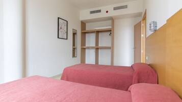 A bedroom with two beds, a wooden wardrobe, and a framed picture on the wall.