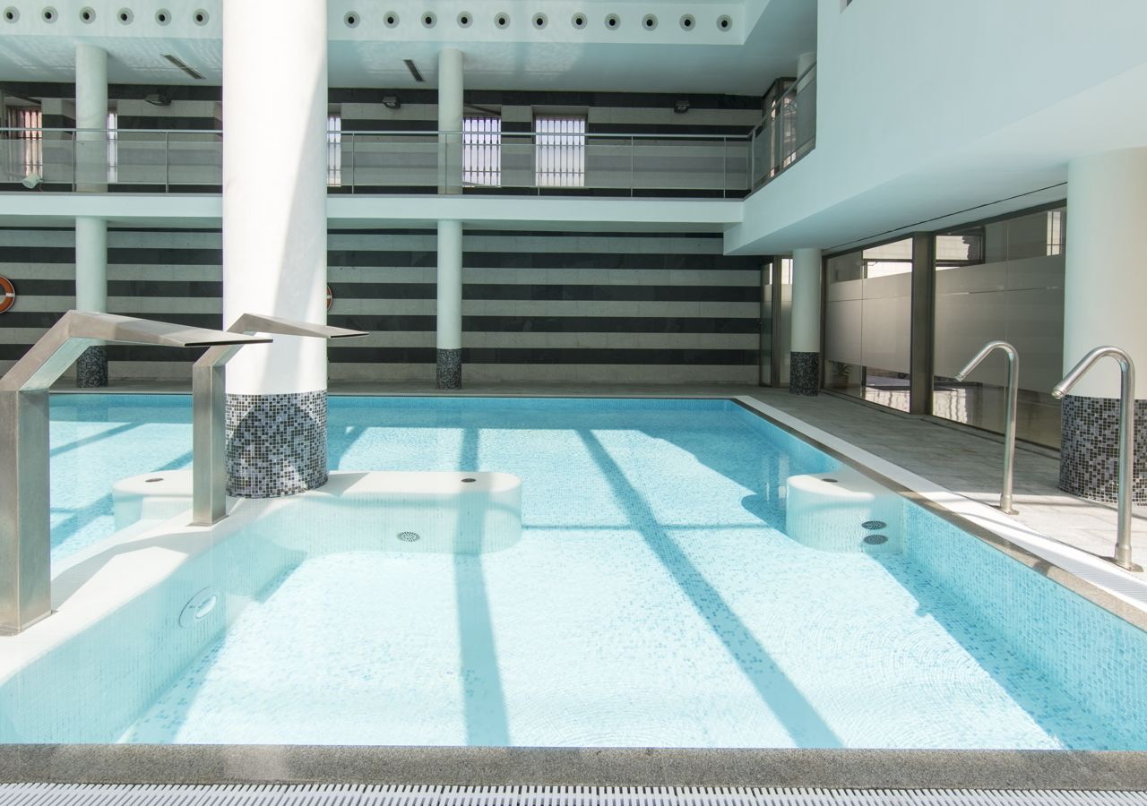 Una piscina interior con agua cristalina, paredes de azulejos y un diseño arquitectónico moderno.