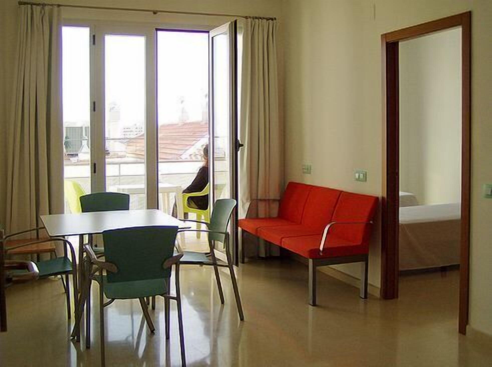 Une pièce comprenant une table à manger, des chaises, un canapé rouge et une porte-fenêtre coulissante donnant sur un espace extérieur.