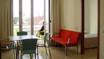 Une pièce comprenant une table à manger, des chaises, un canapé rouge et une porte-fenêtre coulissante donnant sur un espace extérieur.