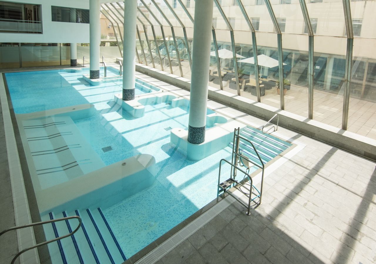 Una piscina interior con carriles delimitados, zona de vestuarios y vistas al exterior a través de amplias ventanas.