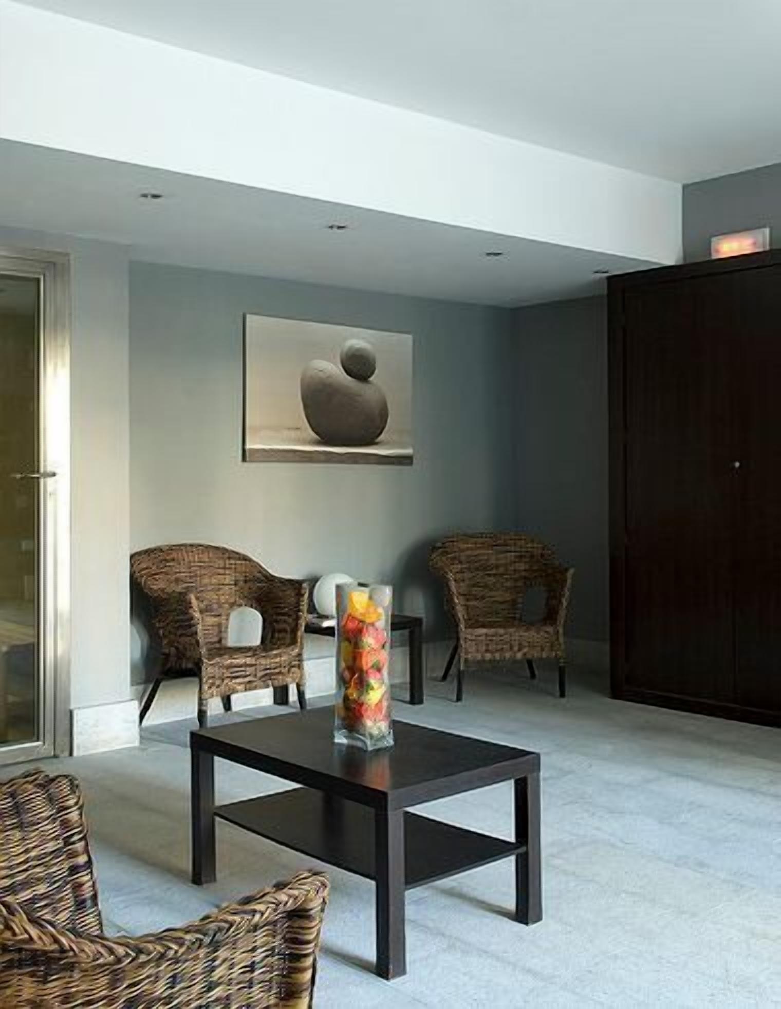 A modern living room with a dark wooden coffee table, wicker chairs, and a painting on the wall.