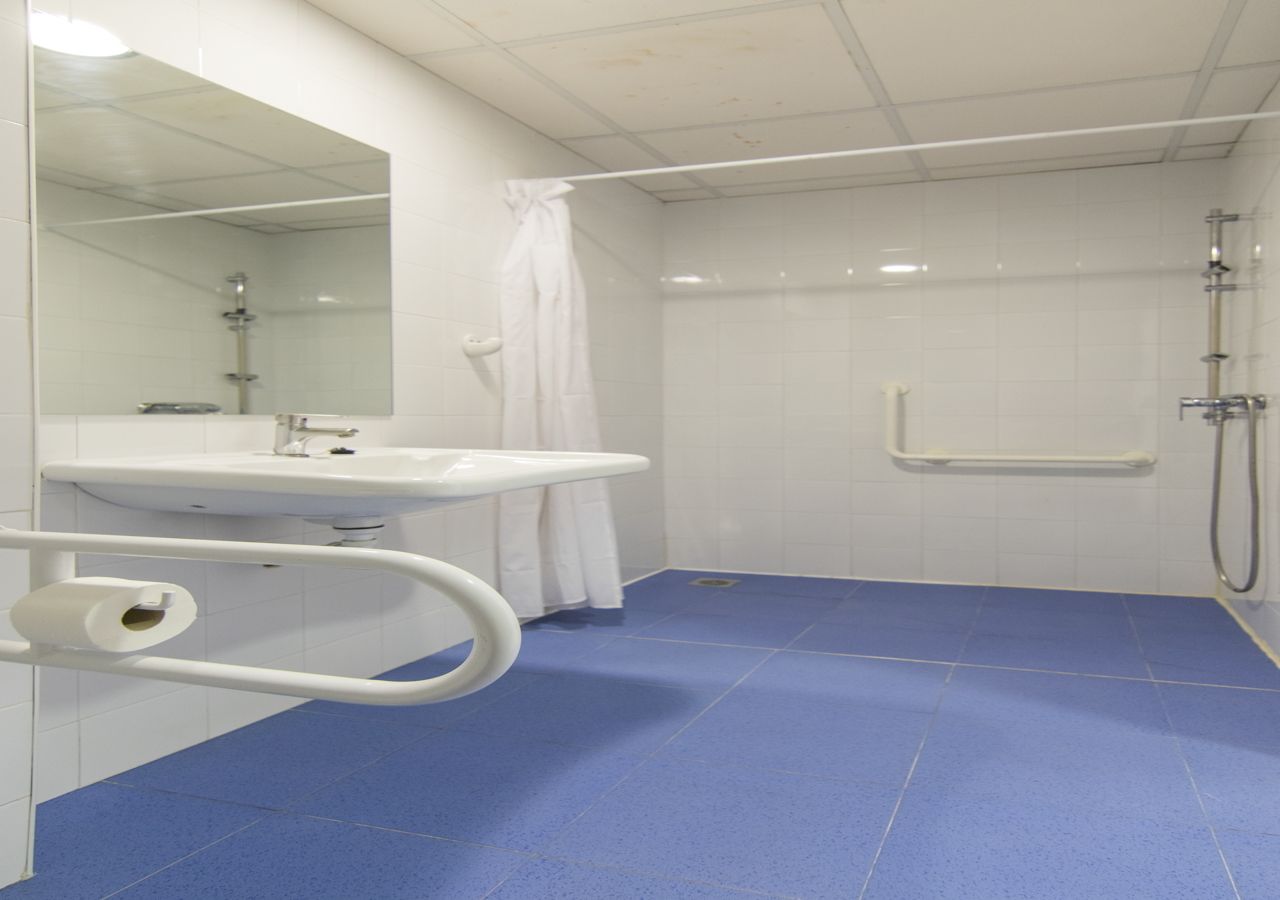 Ein Badezimmer mit einem weißen Waschbecken, einem Spiegel, einer Dusche und einem blauen Boden.