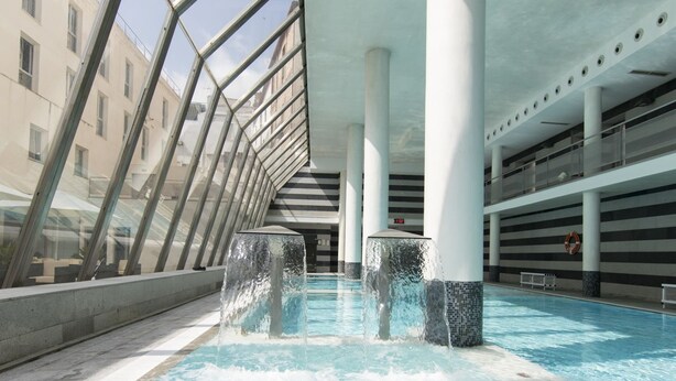 An indoor swimming pool with clear water, surrounded by white columns and glass railings. - Albergue Inturjoven & Jaen - Hostel (Jaén)