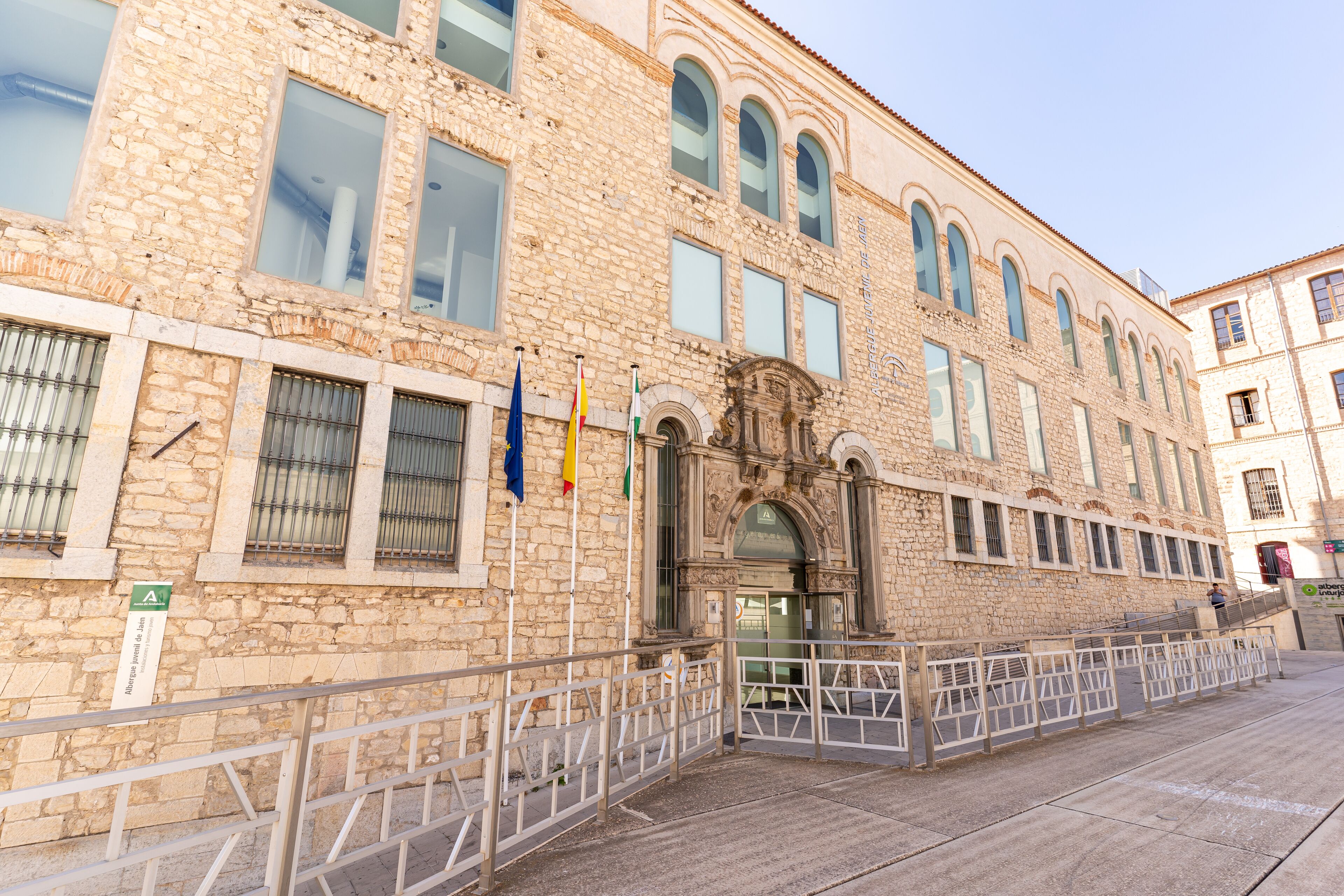 Un edificio histórico de piedra con entrada central, múltiples ventanas y exhibición de banderas.