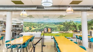 A cafeteria with tables and chairs, a mural of a landscape, and a kitchen area. - Albergue Inturjoven & Jaen - Hostel (Jaén)