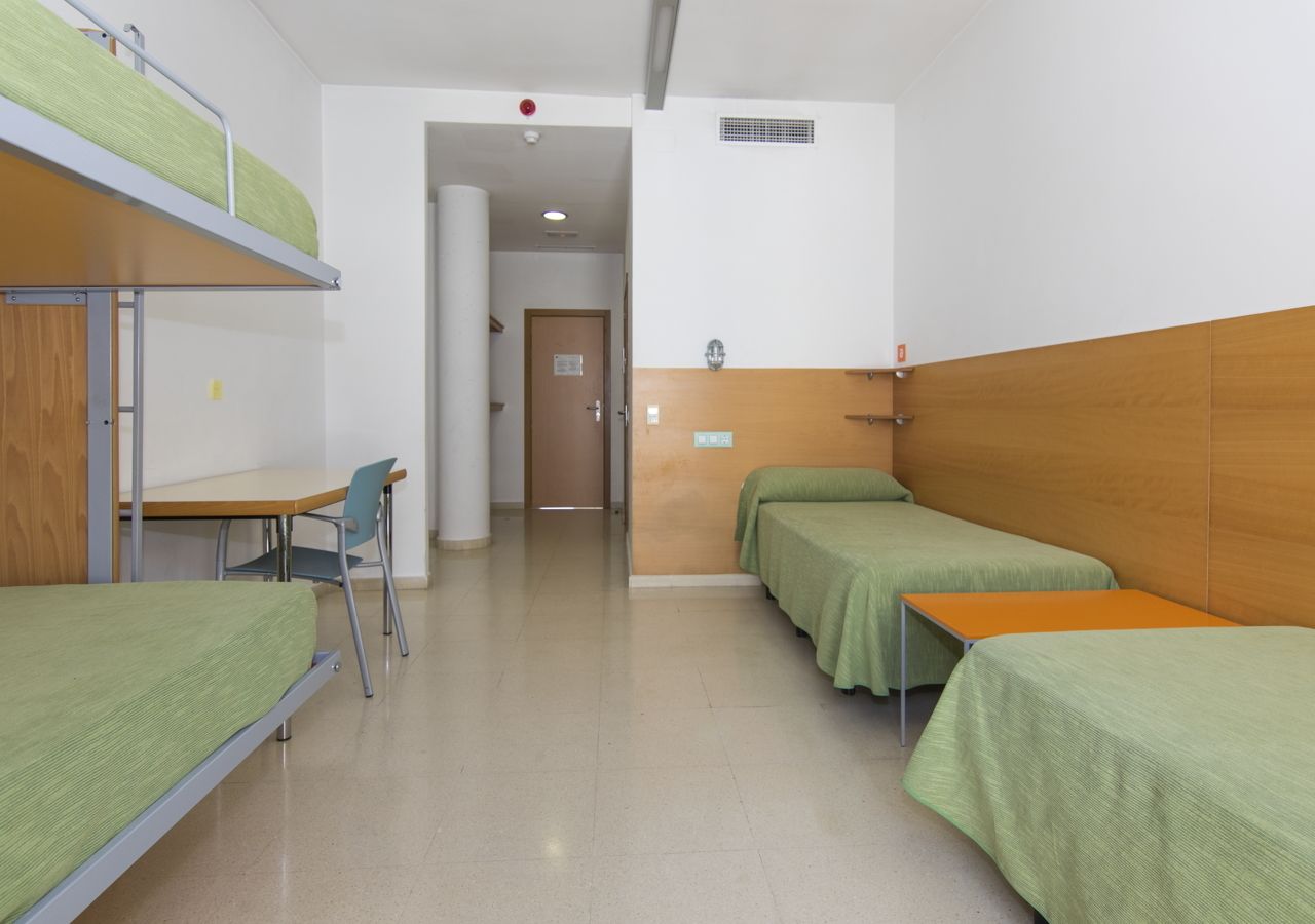 A dormitory room with bunk beds, a desk, and a chair.