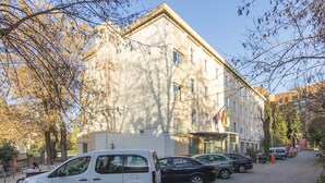 A building with a classic architectural style, featuring a central entrance and multiple windows. There are parked cars along the street in front of the building.