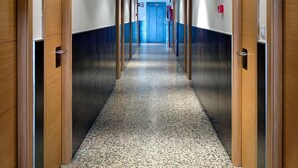 Un largo pasillo estrecho con puertas de madera a ambos lados, que conduce a una puerta azul al final.