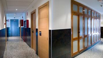 A hallway with a blue elevator, wooden doors, and a tiled floor.