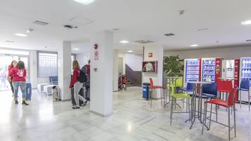 A spacious lobby with a high ceiling, a seating area with colorful chairs, and vending machines.