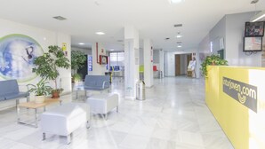Un vestíbulo amplio con una recepción, zona de estar y plantas en macetas.
