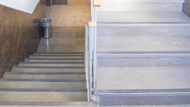 A staircase with a wooden handrail and metal steps, leading to a landing with a door and a fire extinguisher on the wall.