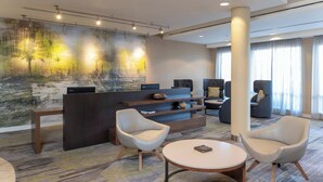 A modern hotel lobby with a reception desk, seating area, and a large abstract mural on the wall. - Courtyard Milwaukee Airport (Milwaukee)