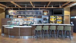 A modern bar area with a wooden counter, bar stools, a menu board, and a variety of beverages. - Courtyard Milwaukee Airport (Milwaukee)