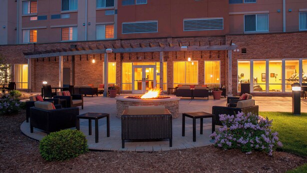 An outdoor patio with wicker furniture, a central fire pit, and a building with multiple windows and a brick facade. - Courtyard Milwaukee Airport (Milwaukee)