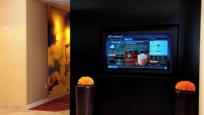 A digital display in a hotel lobby with a GoBoard interface, two dark vases with orange flowers, and a colorful abstract painting on the wall. - Courtyard Milwaukee Airport (Milwaukee)