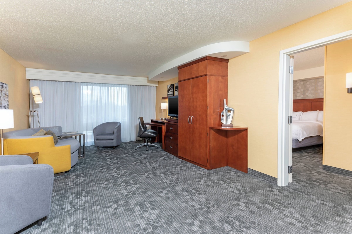 A hotel room with a sofa, armchair, desk, and wardrobe.