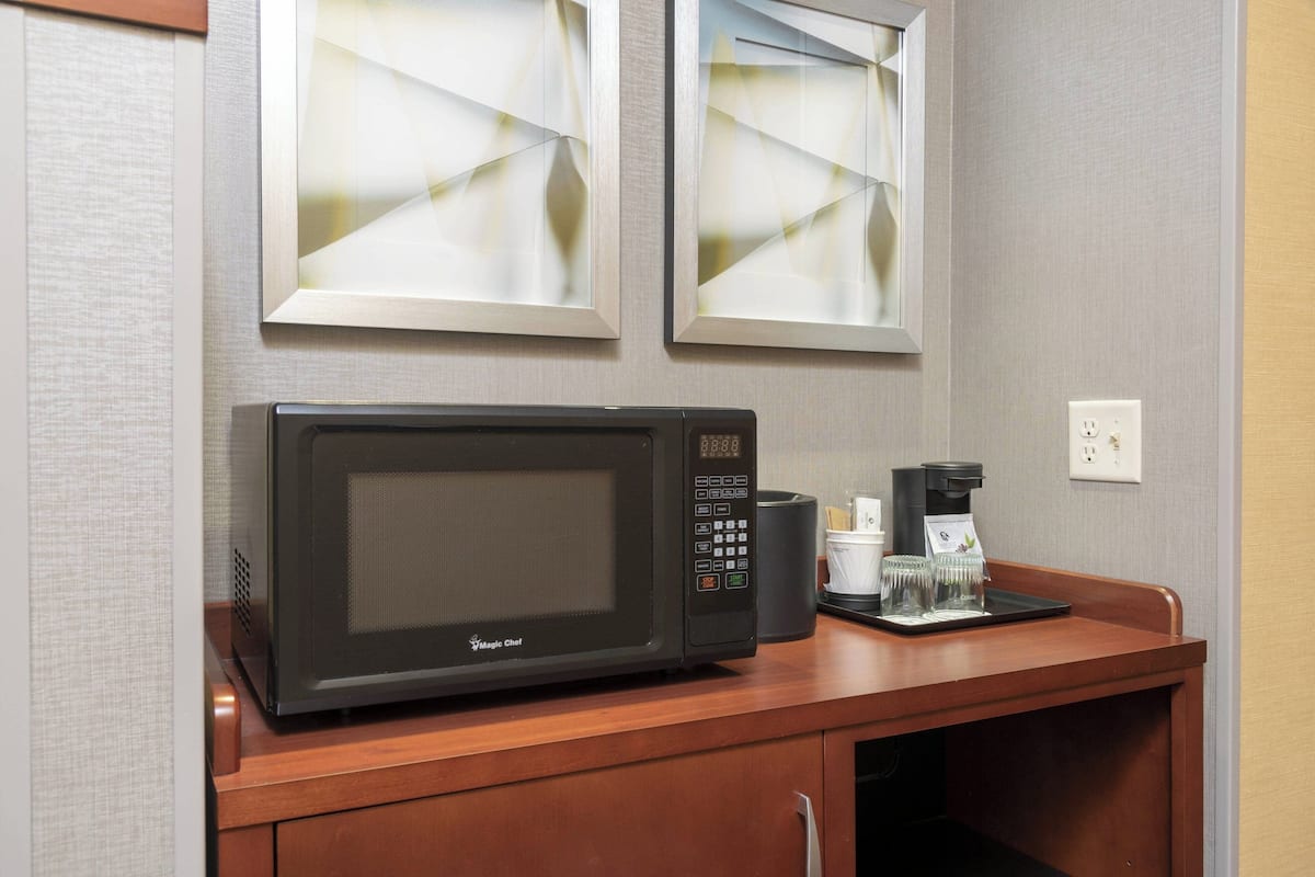 A microwave on a wooden counter with a coffee maker and a glass of water.