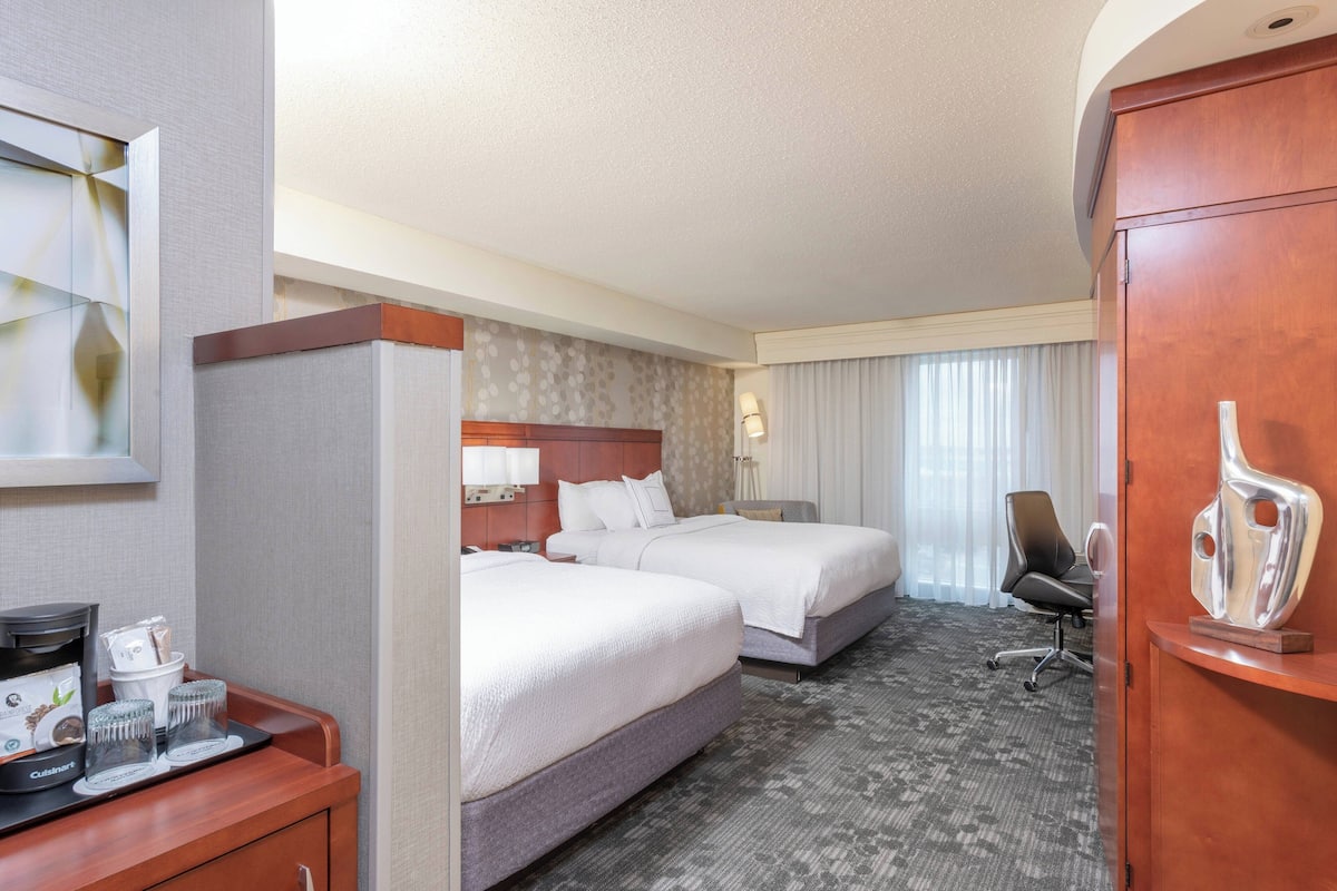A hotel room with two beds, a desk with a coffee maker, and a cabinet.