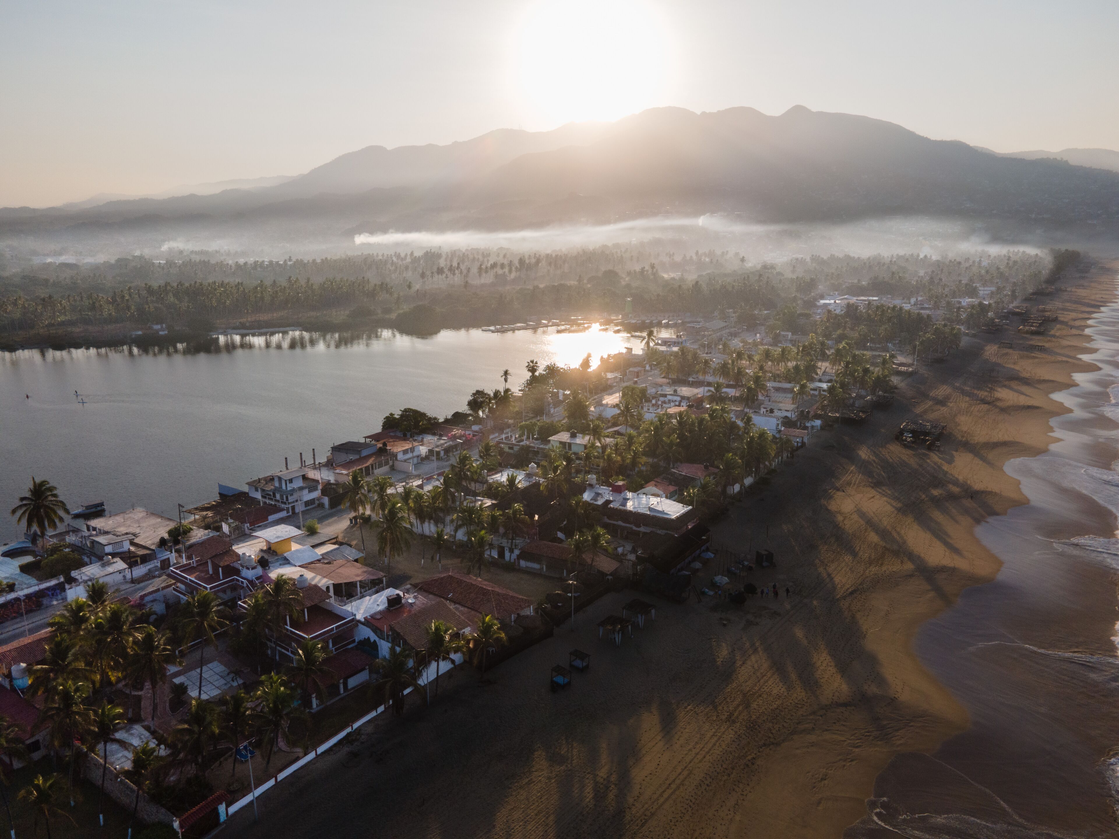 An aerial view of a coastal town with a beach, houses, and a mountain range in the background.