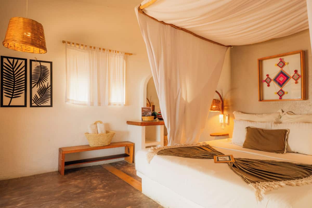 A bedroom with a canopy bed, a bedside table with a basket, and a wall-mounted lamp.