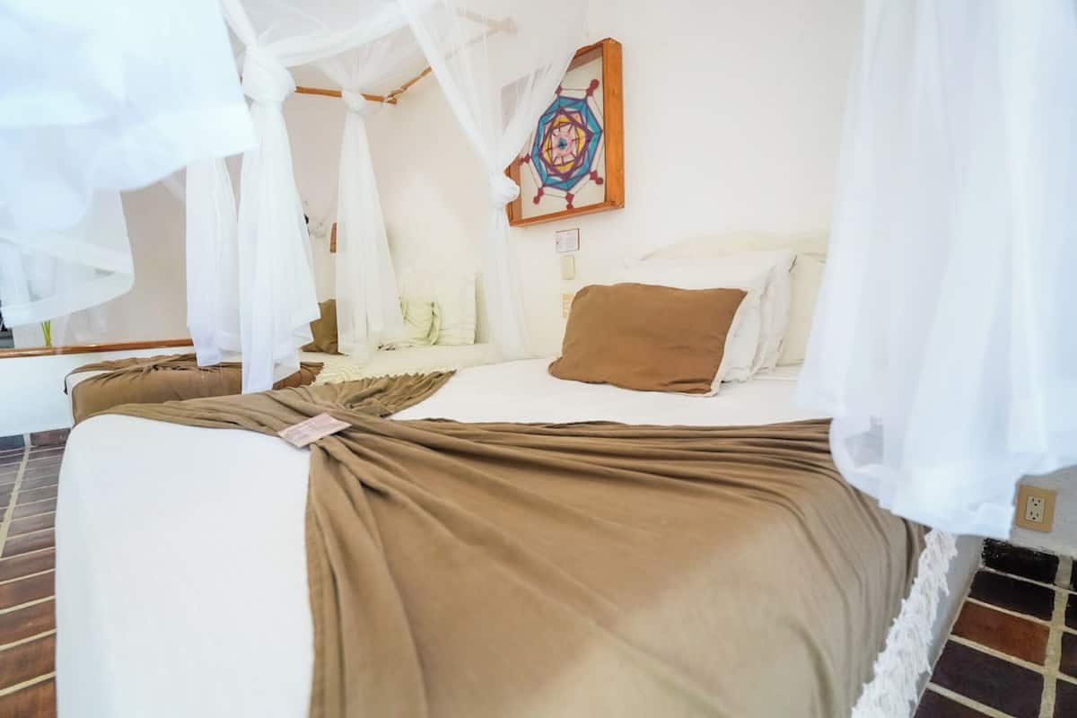 A bedroom with a bed covered in white and brown linens, a canopy, and a wall-mounted artwork.